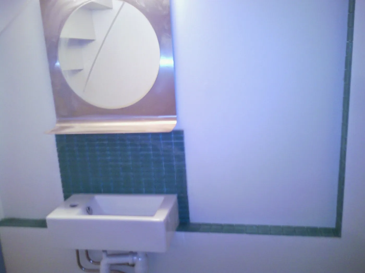Vägghängt tvättställ med rund spegel och mosaikbård i grönt glasmosaik