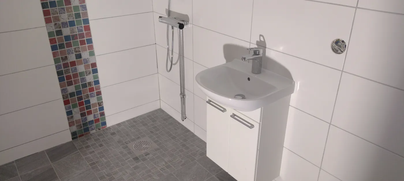 Vitkaklat badrum med lodrät mosaikbård och vägghängt tvättställ