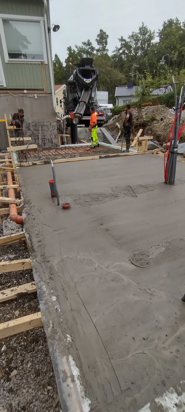 Gjutning av platta pågår, med betongpump och hantverkare på plats