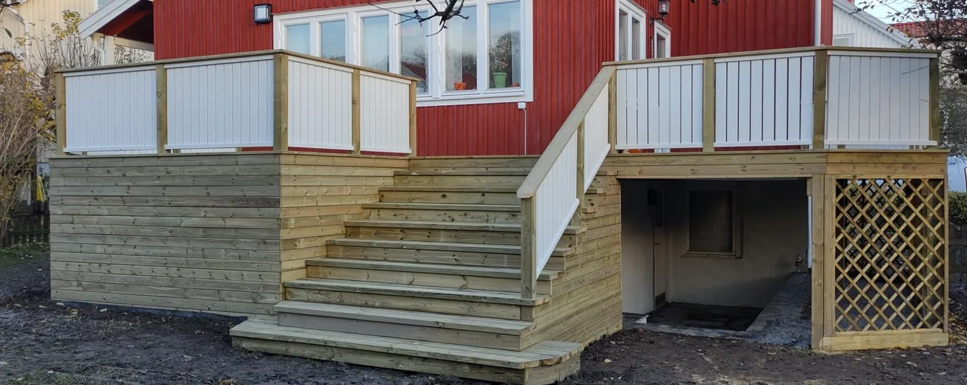 Vitmålat räcke och trappa upp till en altan vid ett rött hus