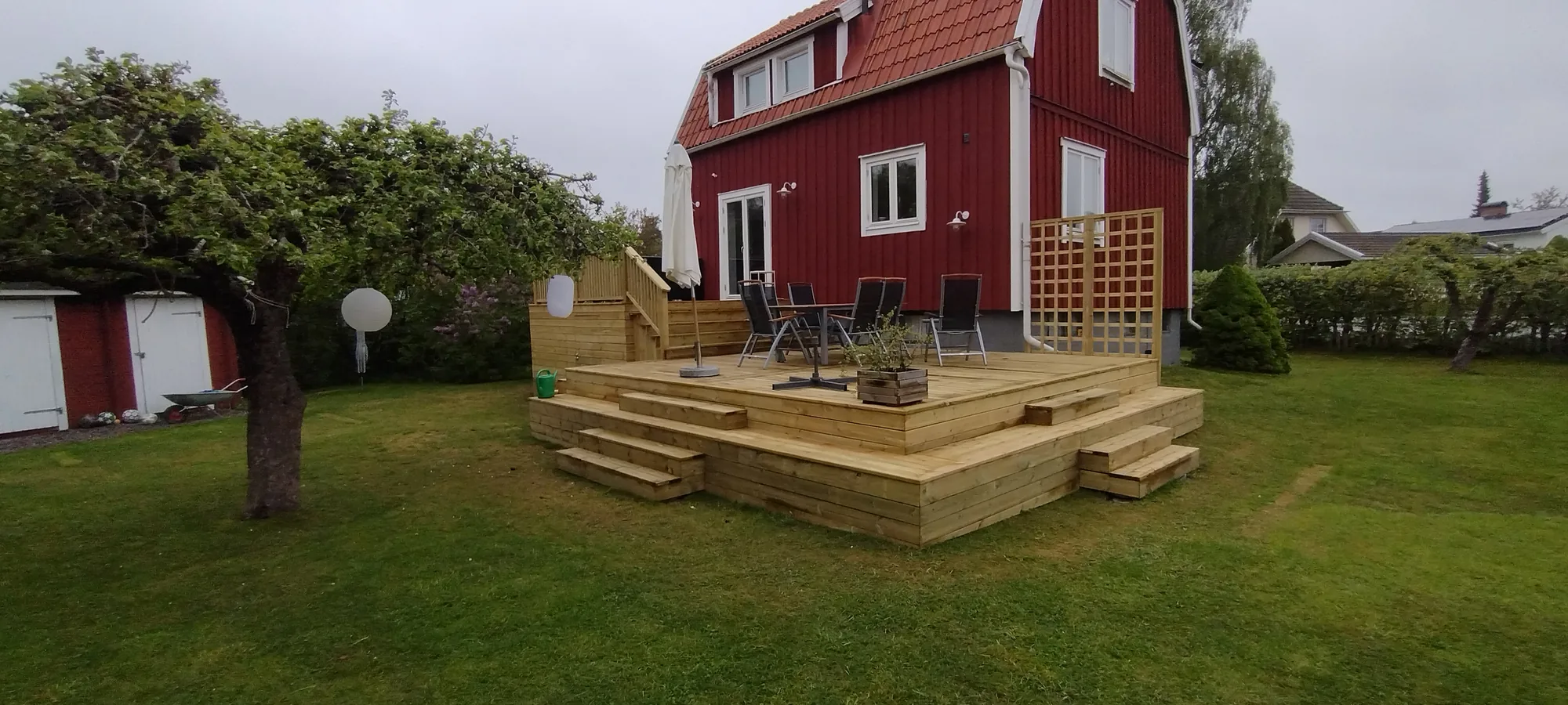 Nybyggd altan i tryckimpregnerat trä framför ett falurött trähus, utförd av Robert’s Hantverks Service