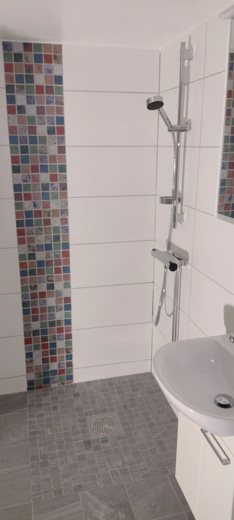 Duschvägg med lodrät rand i flerfärgad mosaik och stengolv
