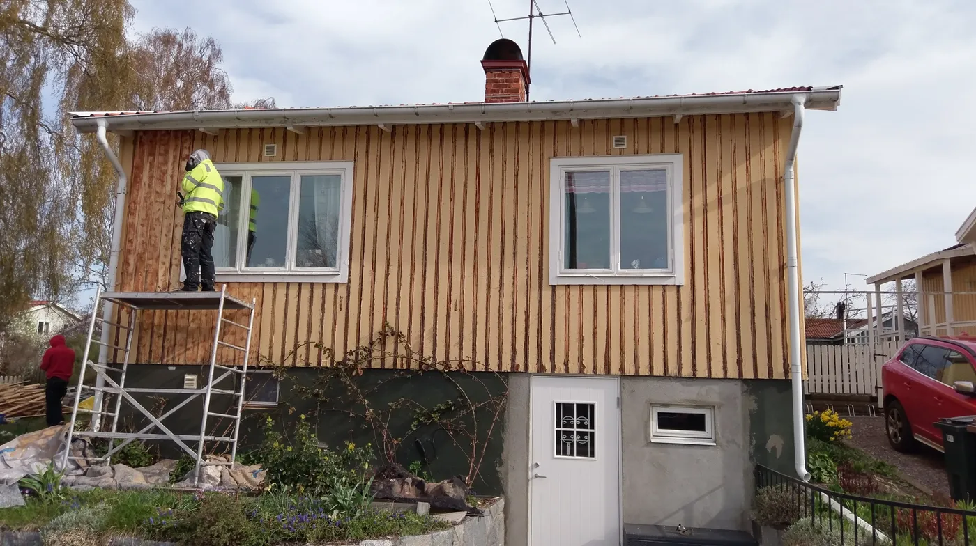 Fasaden fräst ner till rent trä, med hantverkare på ställningstorn