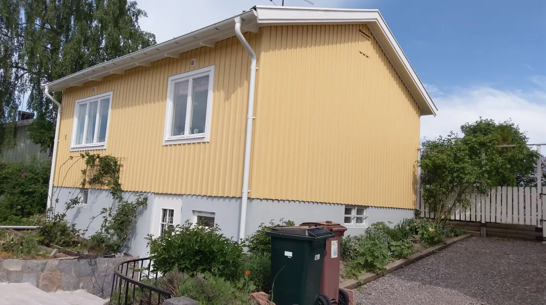 Färdigmålad gul träfasad med vita knutar och nymålad sockel i Bromma