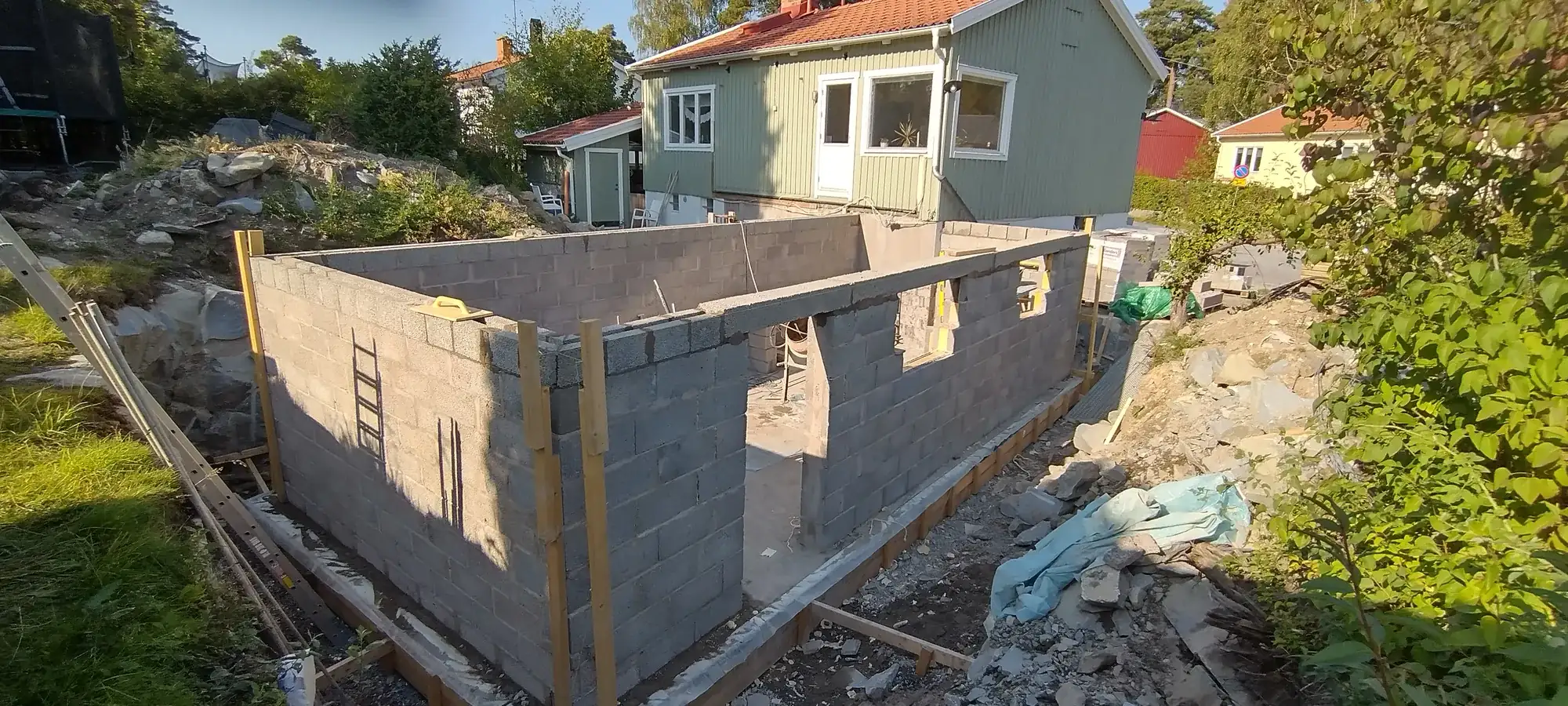 Grundmur i lecablock med gjuten platta för en tillbyggnad intill ett grönt trähus