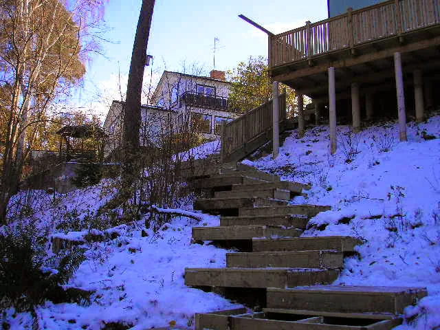 Trätrappa som leder upp genom en snötäckt slänt mot en altan på plintar